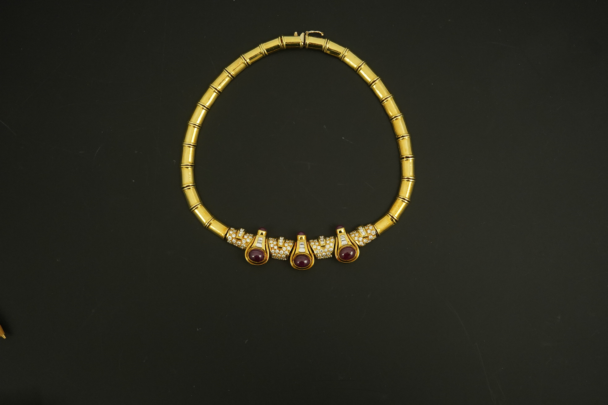 A modern 18k gold, cabochon ruby, round and baguette cut diamond cluster set torque necklace and a pair of matching earrings